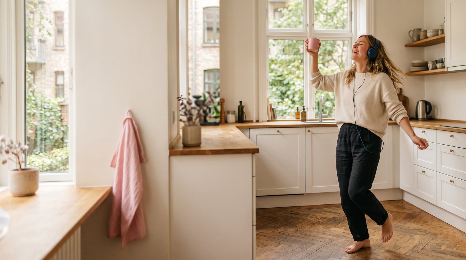 Ung kvinde danser barfodet i sit lyse københavnske køkken med høretelefoner og en kop kaffe.